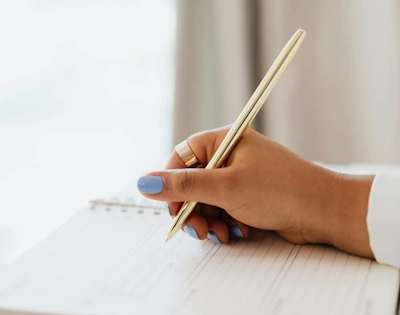 Femme tenant un stylo doré et écrivant dans un carnet, illustrant le service de gestion administrative à Lille d'Anne-Sophie Billaud