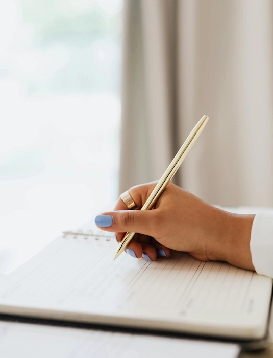 Femme tenant un stylo doré et écrivant dans un carnet, illustrant le service de gestion administrative à Lille d'Anne-Sophie Billaud