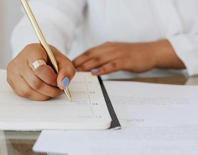 Femme écrivant dans un carnet avec un stylo doré représentant le service de gestion commerciale à Lille d'Anne-Sophie Billaud