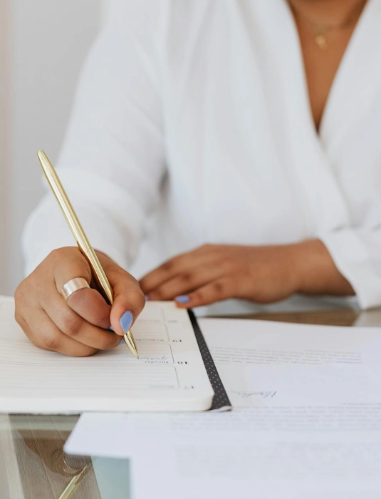 Femme écrivant dans un carnet avec un stylo doré représentant le service de gestion commerciale à Lille d'Anne-Sophie Billaud