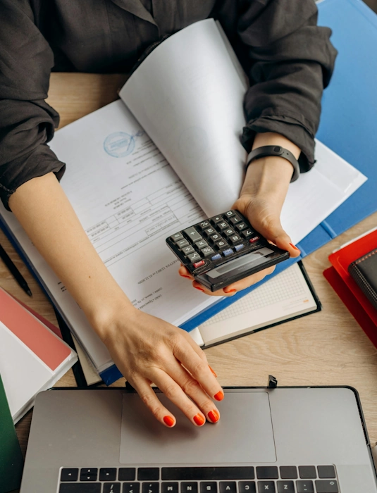 Femme tenant une calculatrice près d'un ordinateur portable, représentant le service de précomptabilité à Lille d'Anne-Sophie Billaud