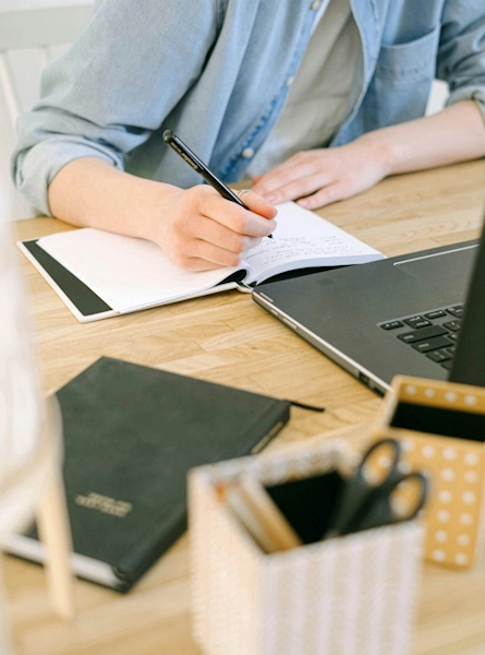 Assistante administrative indépendante à Lille représentée par une femme écrivant dans un carnet, sur un bureau avec un ordinateur et un agenda.